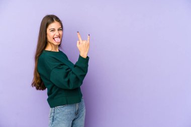 Mor arka planda izole edilmiş genç beyaz kadın parmaklarıyla taş hareketi gösteriyor.