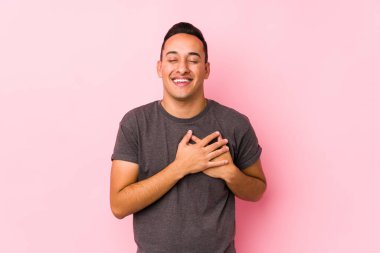 Pembe arka planda poz veren yog latin adam gülüyor, ellerini kalbe koyuyor, mutluluk kavramını koruyor..