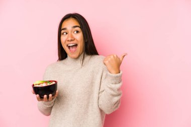 Genç Asyalı bir kadın erişte tutuyor başparmağı uzakta, gülerek ve kaygısızca..