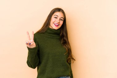 Beyazlı genç bir kadın bej arka planda izole edilmiş zafer işareti gösteriyor ve gülümsüyor..