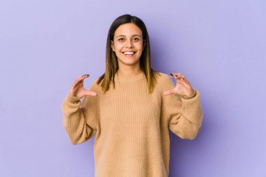 Mor arka planda izole edilmiş genç bir kadın elinde avuç içi bir şeyle kameraya sunuyor..