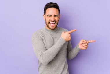 Mor arka planda izole edilmiş genç beyaz adam işaret parmağıyla fotokopi alanını işaret ederek heyecan ve arzusunu ifade ediyor..