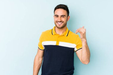 Mavi arka planda izole edilmiş genç beyaz bir adam bir şeye gülüyor, ağızlarını ellerle kapatıyor..