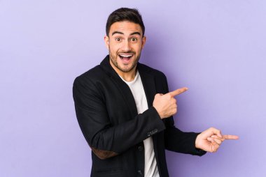 Mor arka planda izole edilmiş genç beyaz adam işaret parmağıyla işaret ederek heyecanlanıyor..