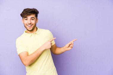 Mor bir arka planda izole edilmiş genç bir Arap işaret parmaklarıyla işaret ederek heyecanlanıyor..