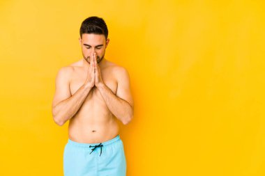 Sarı arka planda mayosu olan genç, beyaz tenli, kendini adamış, dindar, kutsal ilhamı arayan beyaz bir adam..