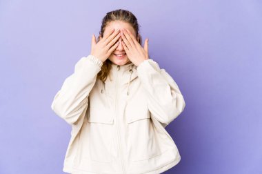 Mor arka plandaki genç beyaz kadın elleriyle gözlerini kapatıyor, geniş bir gülümsemeyle bir sürpriz bekliyor..