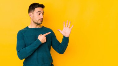 Sarı fırında izole edilmiş genç beyaz adam gülümseyerek beş numarayı parmaklarıyla gösteriyor..