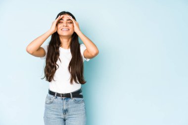 Mavi arka plandaki genç Hintli kadın ellerini başının üstünde tutarak gülüyor. Mutluluk kavramı.