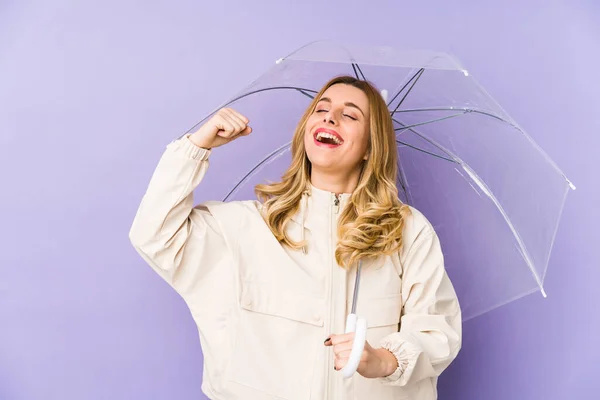 Young blonde woman holding an umbrella isolated Young blonde woman holding an umbrella isolated raising fist after a victory, winner concept.