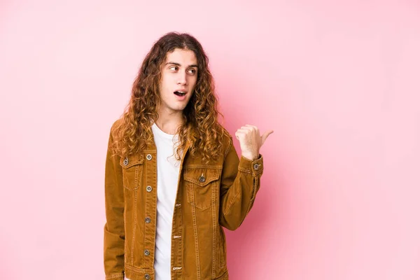 Young long hair man posing isolated points with thumb finger away, laughing and carefree.