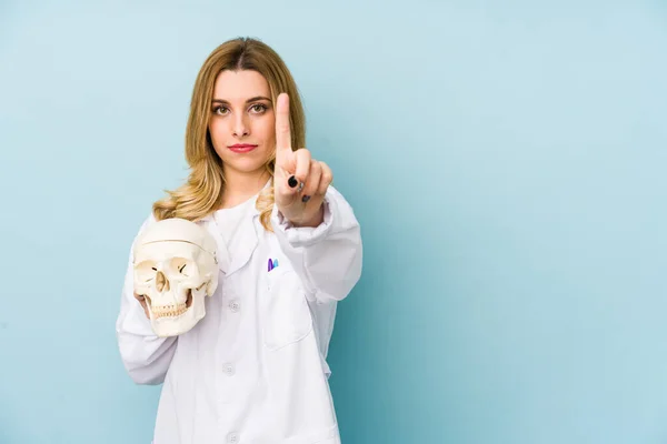Young doctor woman holding a skull isolated showing number one with finger.