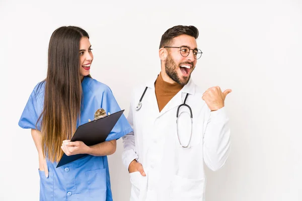 Young doctor man and a nurse isolated points with thumb finger away, laughing and carefree.