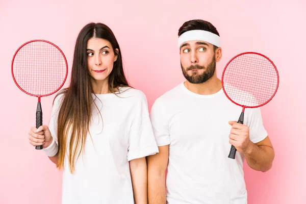 Casal Jovem Jogando Badminton Isolado Confuso Sente Duvidoso Inseguro — Fotografia de Stock