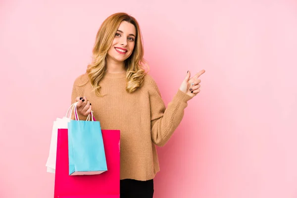 Ung Blond Kvinna Håller Shoppingpåsar Isolerade Leende Och Pekar Sidan — Stockfoto