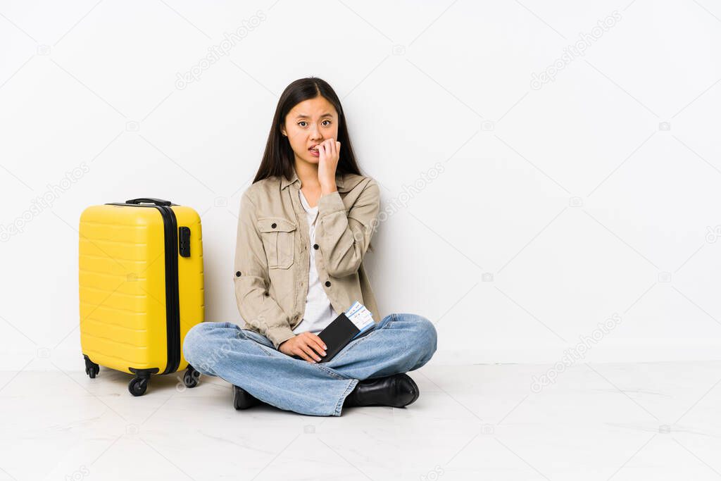 Young chinese traveler woman sitting holding a boarding passes biting fingernails, nervous and very anxious.