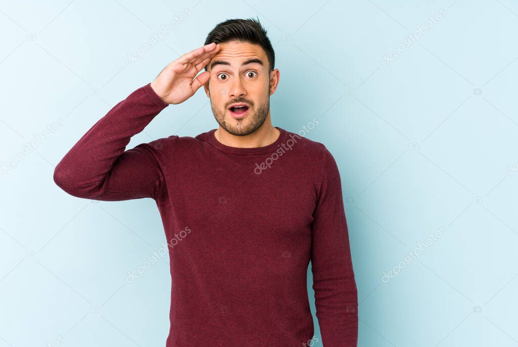 Young caucasian man isolated on blue background shouts loud, keeps eyes opened and hands tense.