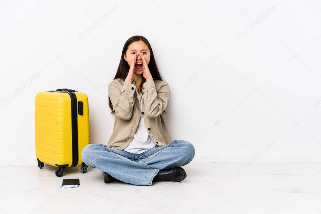 Young chinese traveler woman sitting holding a boarding passes shouting excited to front.