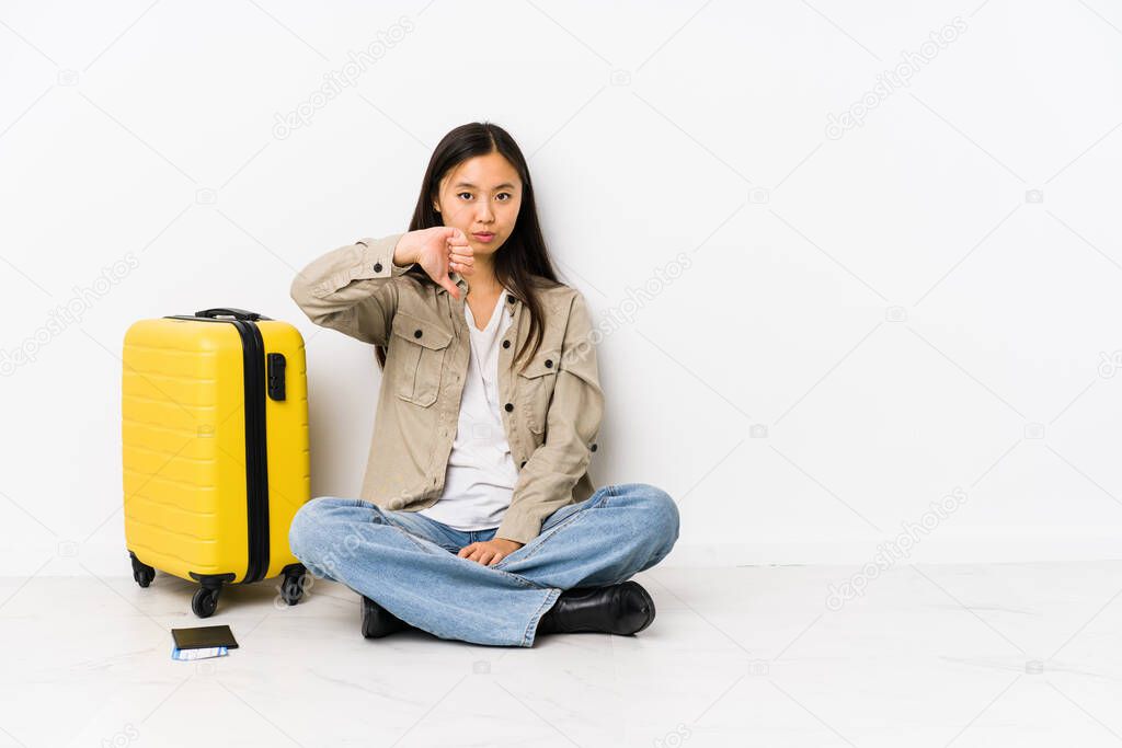 Young chinese traveler woman sitting holding a boarding passes showing a dislike gesture, thumbs down. Disagreement concept.