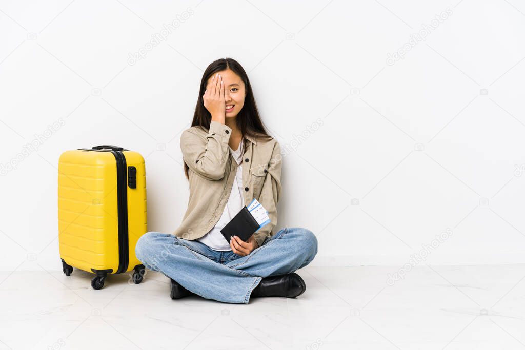 Young chinese traveler woman sitting holding a boarding passes having fun covering half of face with palm.