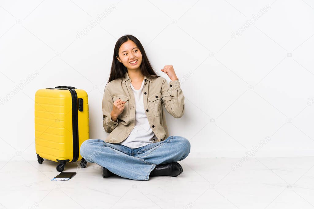 Young chinese traveler woman sitting holding a boarding passes raising fist after a victory, winner concept.
