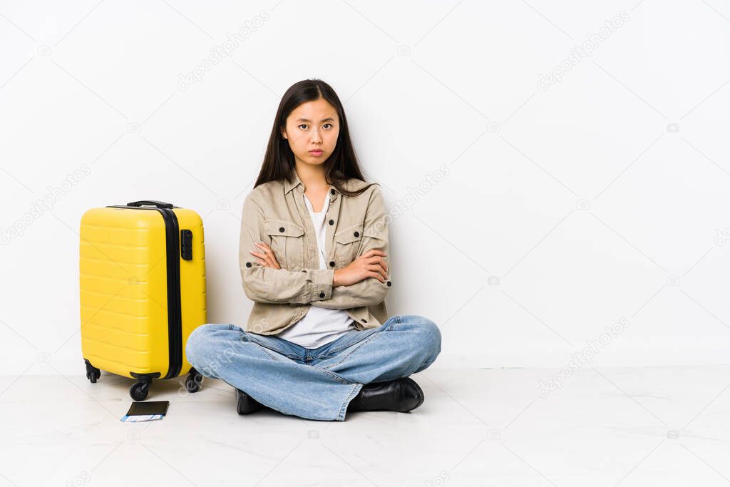 Young chinese traveler woman sitting holding a boarding passes frowning face in displeasure, keeps arms folded.