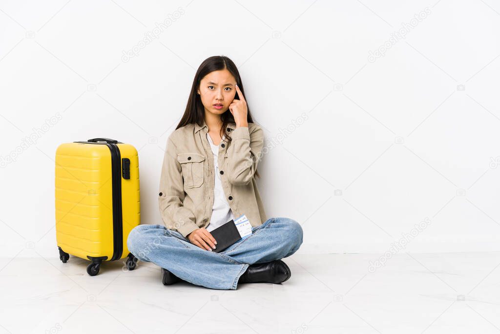 Young chinese traveler woman sitting holding a boarding passes showing a disappointment gesture with forefinger.