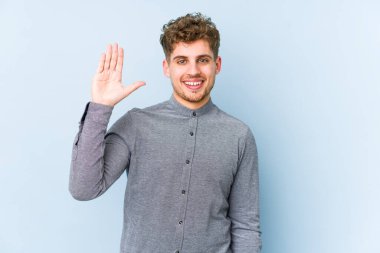 Sarışın, kıvırcık saçlı, beyaz tenli bir adam izole edilmiş gülümseyen beş numarayı parmaklarıyla gösteriyor..