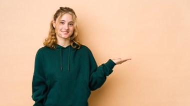 Beyaz tenli genç bir kadın, bej arka planda izole edilmiş bir şekilde bir avuç içinde fotokopi alanı ve belinde bir el daha gösteriyor..