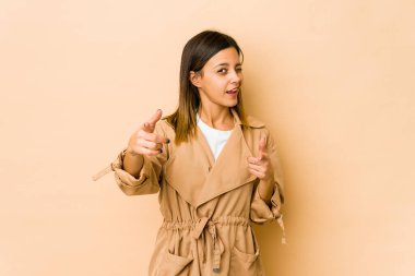 Bej arka planda izole edilmiş genç bir kadın parmaklarıyla ön tarafı işaret ediyor..