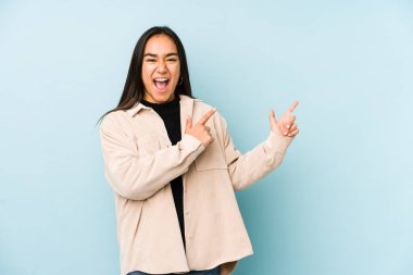 Mavi bir arka planda izole edilmiş genç bir kadın işaret parmaklarıyla fotokopi alanını işaret ederek heyecan ve arzusunu ifade ediyor..