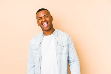 Genç Latin bir adam bej arka planda izole edilmiş komik ve dost canlısı bir dil kullanıyor..