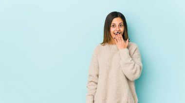 Mavi arka planda izole edilmiş genç bir kadın şok olmuş, ağzı ellerle kaplanmış, yeni bir şey keşfetmeye hevesli..