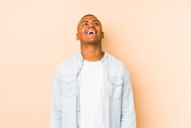 Genç latin adam bej arka planda izole edilmiş gevşemiş ve mutlu bir şekilde gülüyor, boynunda dişlerini gösteriyor..