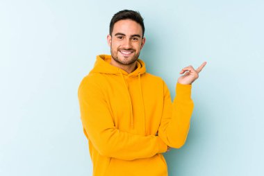 Mavi arka planda izole edilmiş genç beyaz adam işaret parmağıyla işaret ederek gülümsüyor..