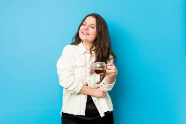 Genç kavisli kadın elinde çay fincanıyla gülüyor ve eğleniyor..