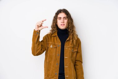 Uzun saçlı adam yalnız poz veriyor. Elinde küçük bir şey tutuyor, gülümsüyor ve kendinden emin..