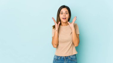 Mavi arka planda izole genç bir kadın şaşırmış ve şok olmuş..