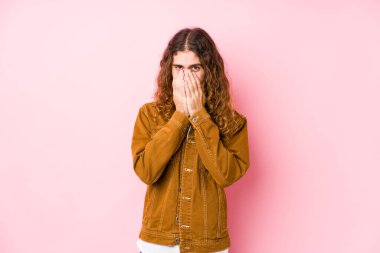 Genç, uzun saçlı adam yalnız poz veriyor. Bir şeye gülüyor, elleriyle ağzını kapatıyor..