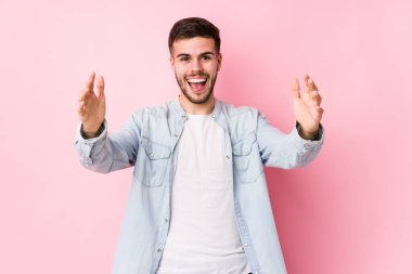 Beyaz arka planda poz veren beyaz tenli genç bir iş adamı hoş bir sürprizle karşılaşıyor, heyecanlı ve el kaldırıyor..