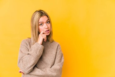 Sarışın, beyaz bir kadın, sarı arka planda izole edilmiş. Rahatlamış, fotokopi odasına bakan bir şey düşünüyor..