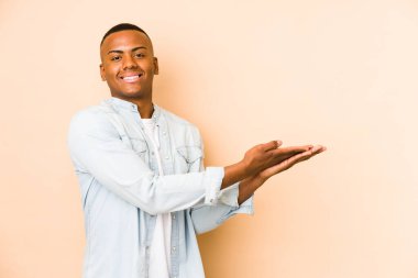 Bej arka planda izole edilmiş genç latin adam palmiye ağacında bir kopya alanı tutuyor..