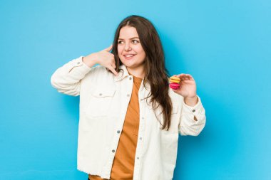 Elinde badem kurabiyesi tutan, cep telefonu hareketini parmaklarıyla gösteren kıvrımlı bir kadın..