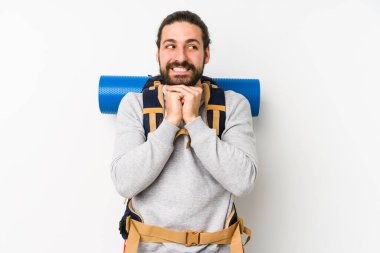 Beyaz arka planda izole edilmiş genç bir sırt çantalı adam ellerini çenesinin altında tutuyor ve mutlu bir şekilde yan tarafa bakıyor..