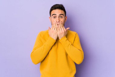 Mor arka planda izole edilmiş genç beyaz adam şok olmuş, ağzı ellerle kaplanmış, yeni bir şey keşfetmeye hevesli..