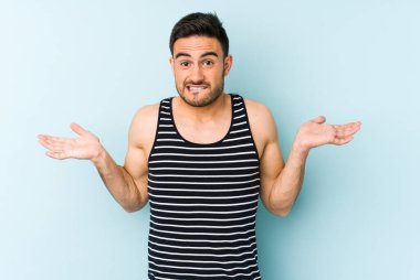 Kafkasyalı genç adam mavi arka planda izole edilmiş. Kafası karışmış ve omuz silkiyor. Kopya alanını tutmak için..
