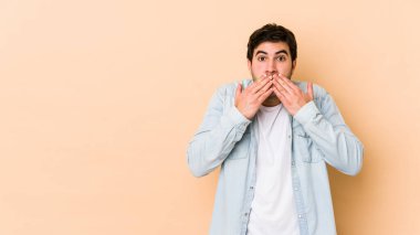 Bej arka planda izole edilmiş genç adam elleriyle ağzını kapatırken şok oldu..