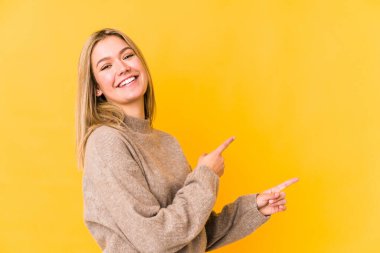 Sarışın, beyaz bir kadın sarı arka planda izole edilmiş. İşaret parmaklarıyla işaret ettiği için heyecanlı..