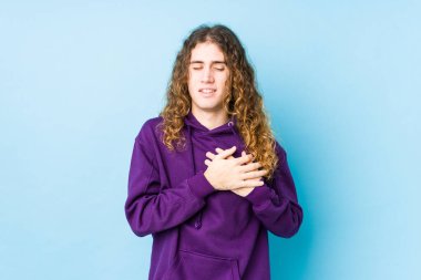 Uzun saçlı adam yalnızmış gibi gülüyor, elleri kalbinde, mutluluk kavramında tutuyor..