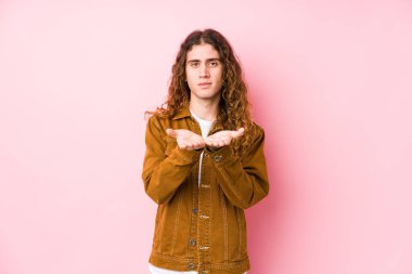 Uzun saçlı genç adam avuçlarıyla bir şey tutarak kameraya poz veriyor..